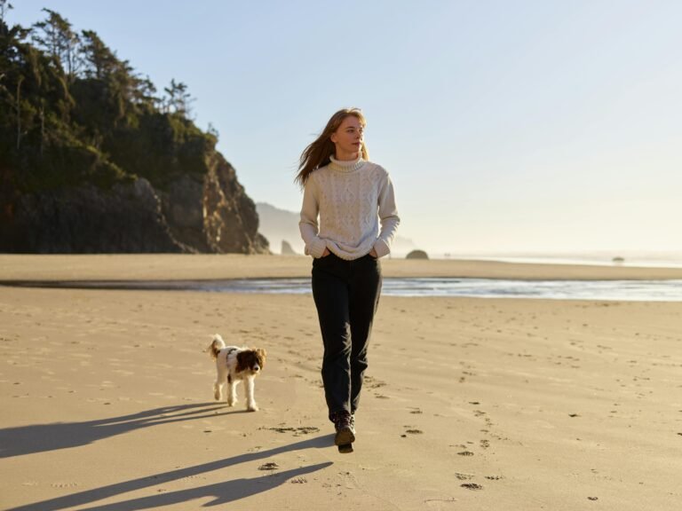 A woman strolls with her dog on a sunny beach, conveying tranquility and freedom.