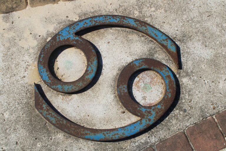 Close-up of a rusted Cancer zodiac symbol on a concrete wall.