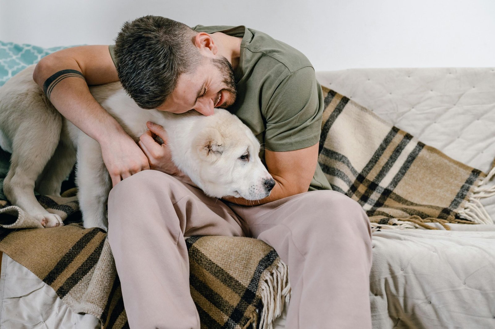 A man lovingly hugs his dog while sitting on a cozy sofa inside a home setting.