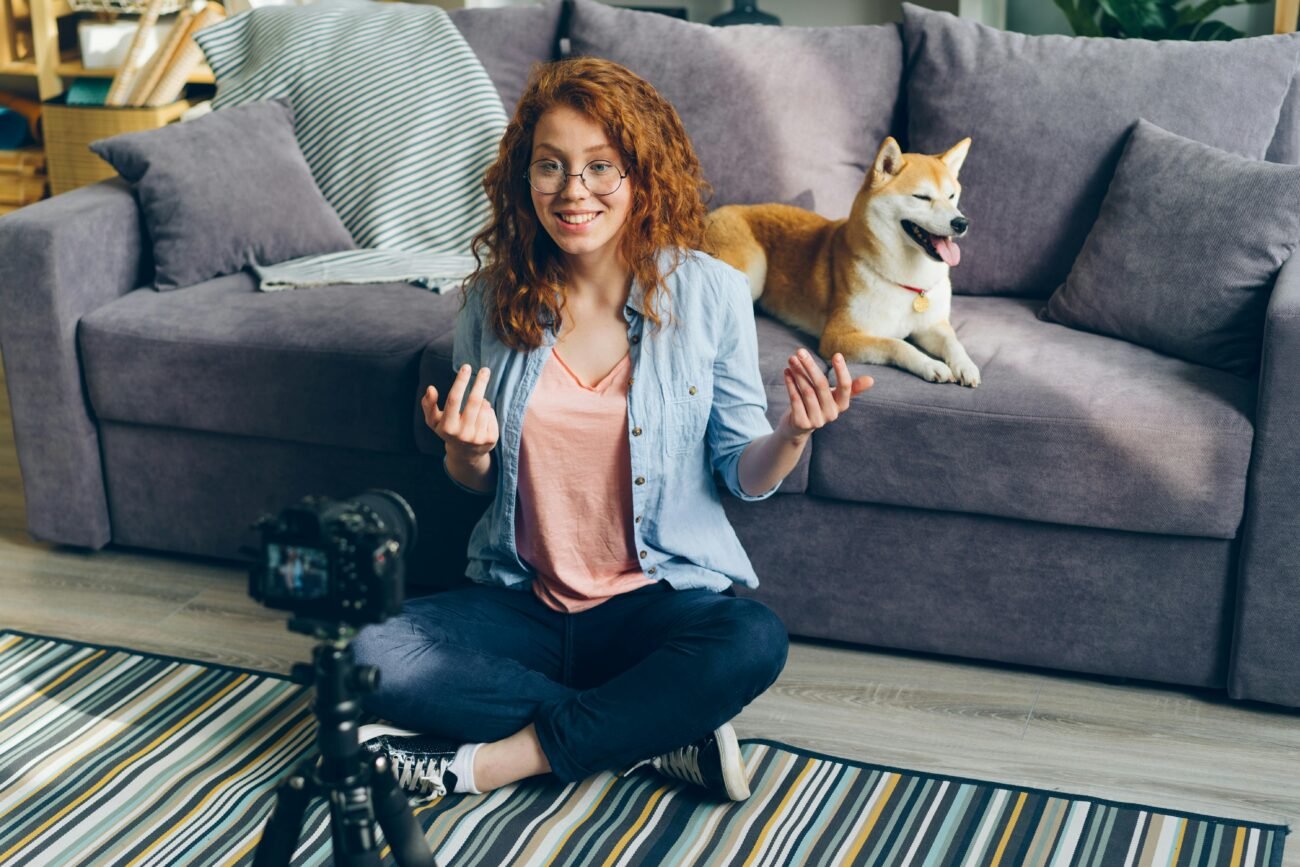 Redhead woman recording a video at home with her Shiba Inu dog on the couch.