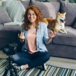Redhead woman recording a video at home with her Shiba Inu dog on the couch.