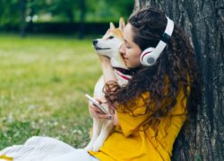 Woman hugging Shiba Inu dog while listening to music in a park.