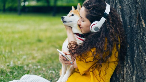 Woman hugging Shiba Inu dog while listening to music in a park.