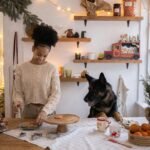 A joyful woman baking cookies with her German Shepherd in a festively decorated kitchen.