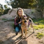 A cheerful woman hiking with her German Shepherd on a sunny day in nature.